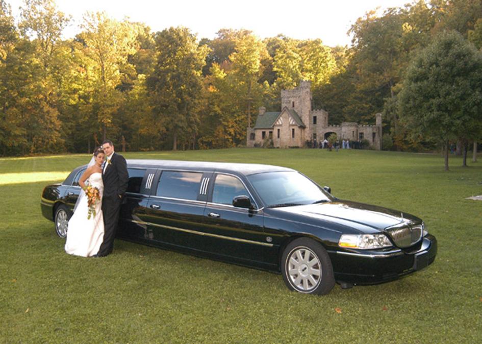 Bride and Groom posing with limousine in front of Squire's Castle