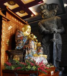 photograph of a golden happy Buddha with a huge statue of a three headed guard watching over at the Chung Tai Chan Monastery in Taiwan